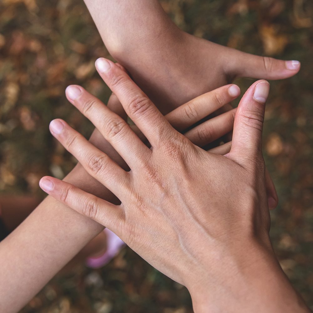 Three hands resting together in a gesture of support and teamwork. No faces shown.