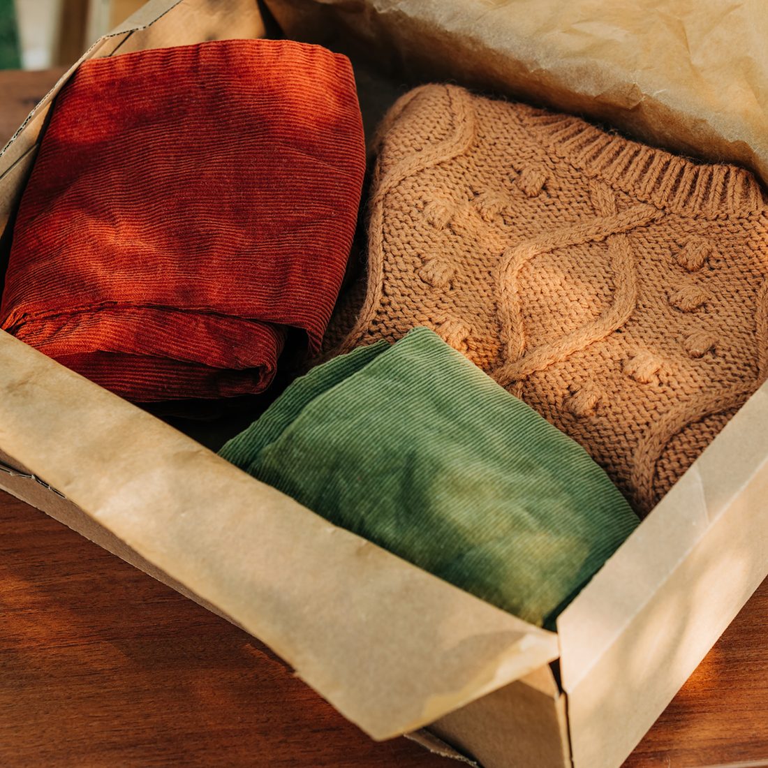 Folded cozy knitwear and corduroy clothing in a box, the kind of gently used goods donations provide. No people shown.