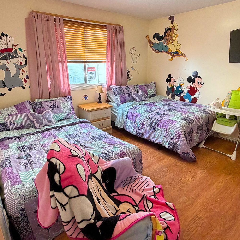 A children's bedroom inside the shelter with two beds, soft bedding, and a warm, welcoming feel. No people shown.
