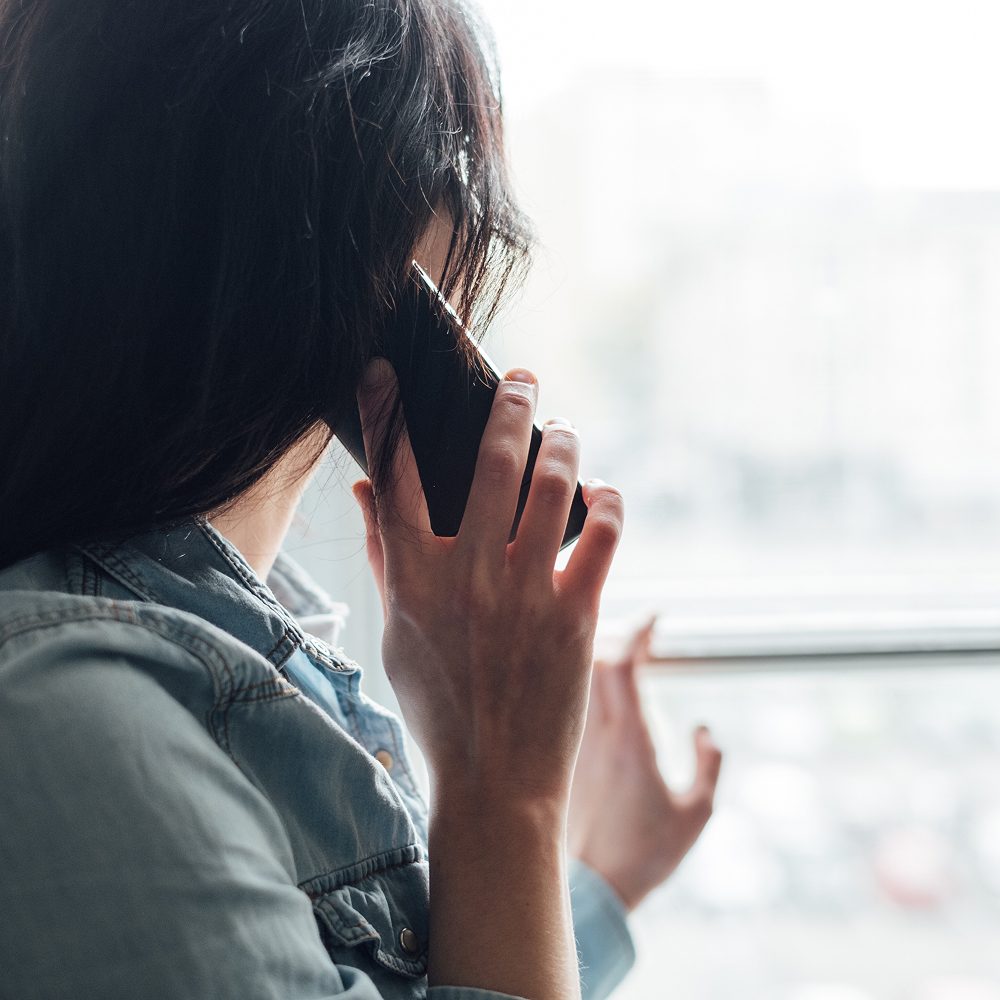 A woman sitting on a park bench making a phone call, seen from behind. No face shown.