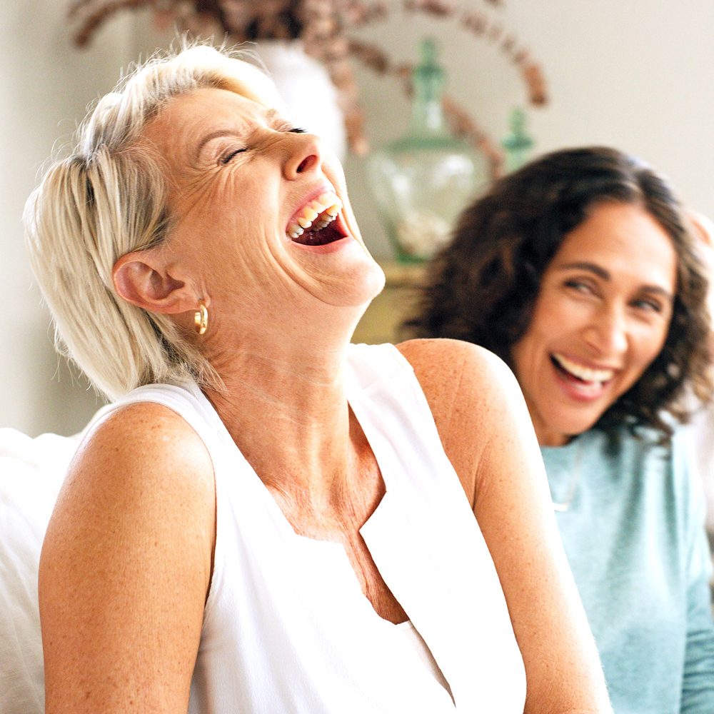 Two women laughing together indoors during a relaxed, friendly get-together.