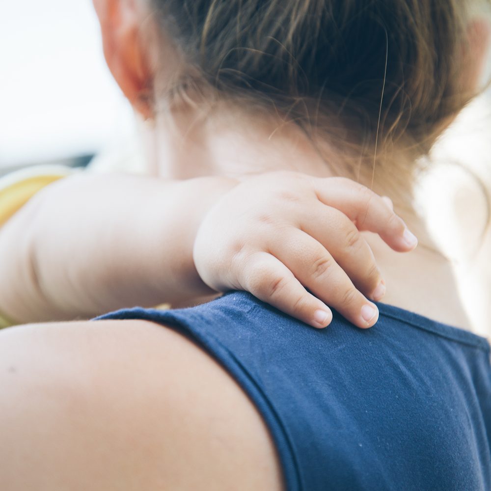 A woman holding her child, seen from behind. No faces shown.